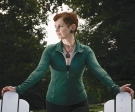 Catherine Waters Raymond, a woman with red hair wearing a green shirt, stands between two white chairs.